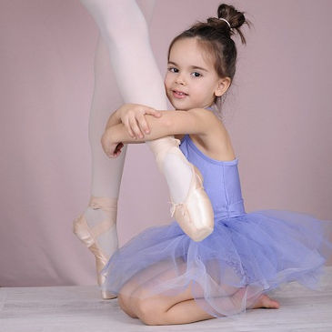 A little girl wearing a lilac tutu holding an adult ballerina's leg