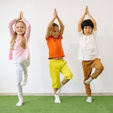 Three children doing the tree yoga pose wearing colourful clothing