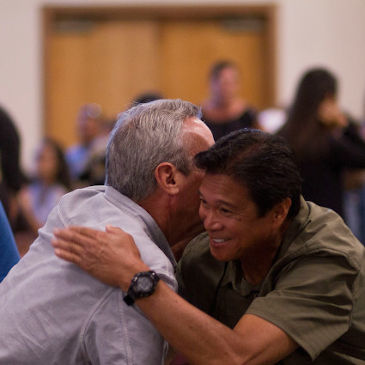 Two men hugging surrounded by a community church congregation
